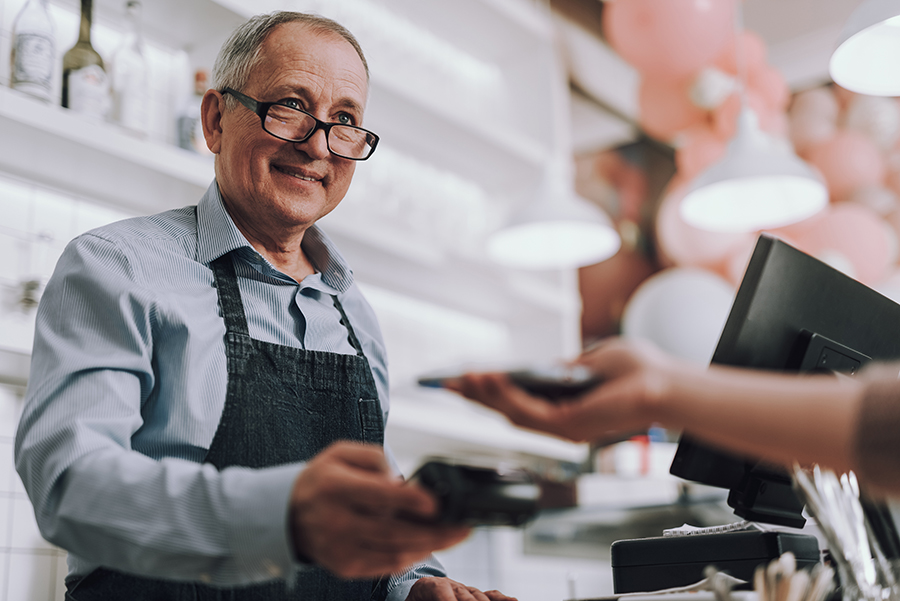 Waist up portrait of good-looking gentleman in apron holding terminal for contactless payment and smiling